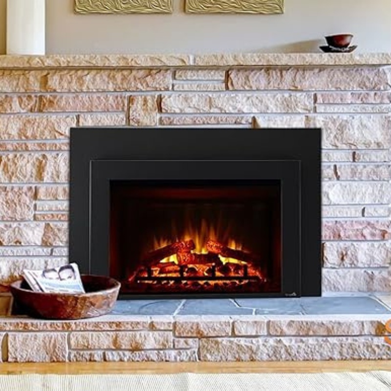 Cozy electric fireplace with glowing logs set in a modern stone mantel, surrounded by decorative wall art and a bowl of magazines on a slate hearth.