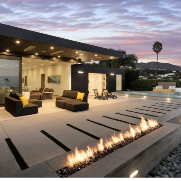 Modern outdoor living space featuring a sleek patio with a fire feature, comfortable seating, and a swimming pool, set against a colorful sunset backdrop.