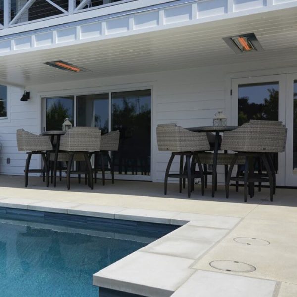 Outdoor dining area with wicker chairs and a table, adjacent to a swimming pool, featuring overhead heating elements for comfort.