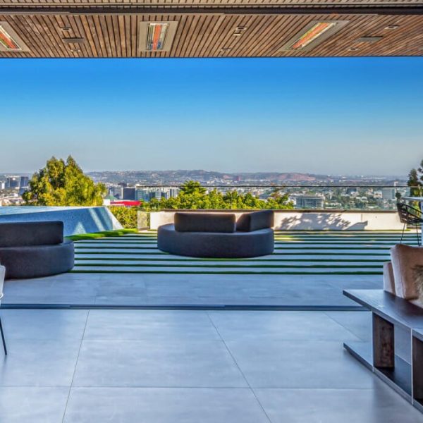 Modern outdoor living space with panoramic city views, featuring circular seating and a sleek design, surrounded by greenery and a swimming pool.