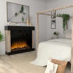 Cozy bedroom featuring a modern electric fireplace, a four-poster bed with white bedding, decorative plants, and framed artwork on the walls, creating a serene atmosphere.