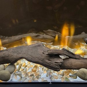 Decorative fireplace featuring glowing flames, driftwood, and colorful glass pebbles for a cozy ambiance.